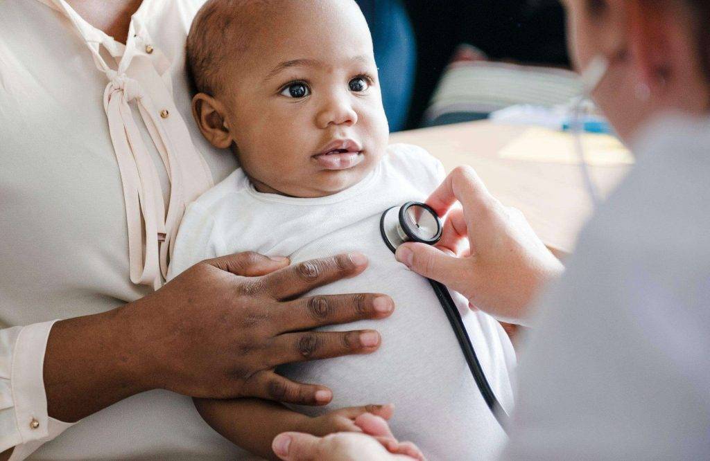 Person holding baby while doctor uses stethoscope