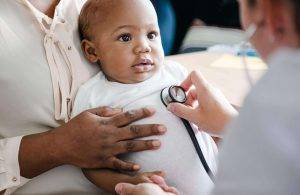 Person holding baby while doctor uses stethoscope
